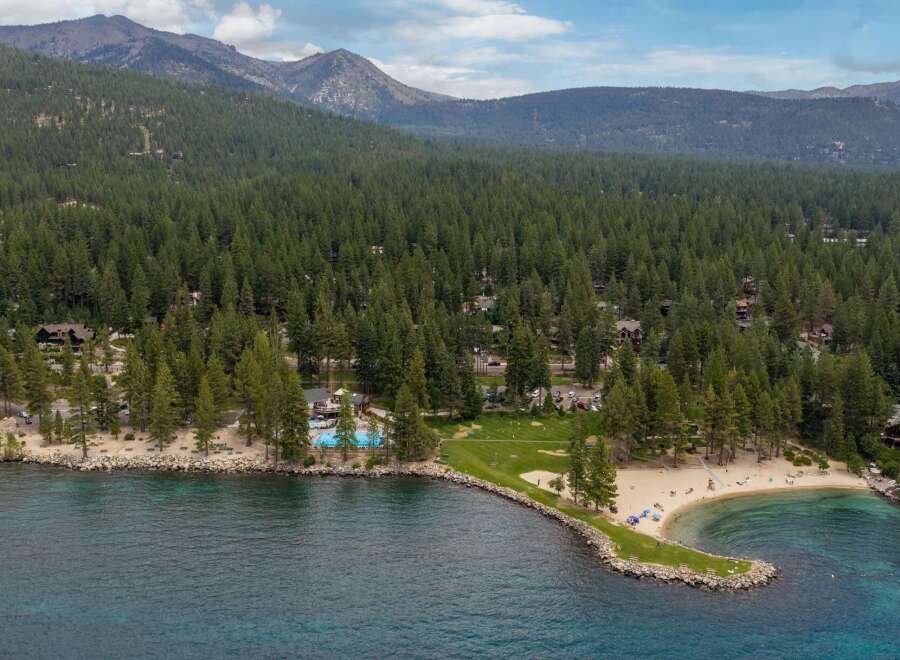 Experience lakeside luxury with this stunning aerial view of a property featuring a private beach, sparkling swimming pool, and lush green spaces perfect for recreation.