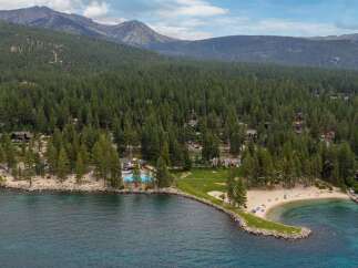 Experience lakeside luxury with this stunning aerial view of a property featuring a private beach, sparkling swimming pool, and lush green spaces perfect for recreation.