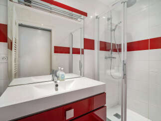 This modern bathroom features a sleek white vanity with a red cabinet, complemented by a large mirror and a stylish chrome faucet.