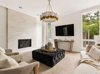 Experience modern luxury in this stunning living room, featuring a dramatic marble fireplace and a stylish tufted ottoman.