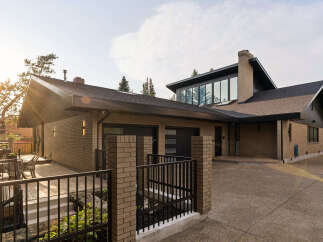 This stunning modern home features a striking brick exterior and a multi-level roofline, complemented by a spacious driveway and an inviting patio area.