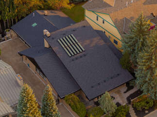 This aerial view showcases a modern home with a dark asphalt shingle roof, featuring multiple skylights and a unique solar panel array.