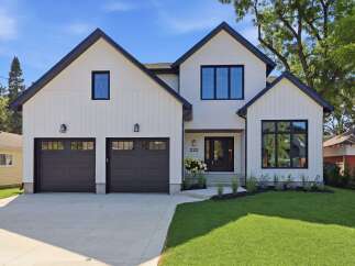 Discover modern living in this stunning white farmhouse-style home featuring a sleek black roof and matching window frames.