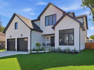 Discover modern living in this stunning white farmhouse-style home featuring a sleek black roof and matching window frames.