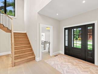 Step into a grand entryway featuring a stunning wooden staircase with black railings and a large window overlooking lush greenery.