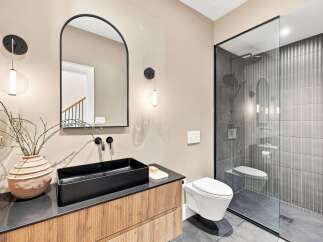 Experience modern luxury in this stunning bathroom featuring a sleek black vessel sink atop a warm wood vanity.
