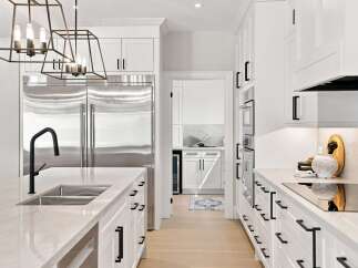 Experience modern luxury in this stunning white kitchen, featuring sleek cabinetry, a large stainless steel refrigerator, and a spacious island with a contemporary black faucet.