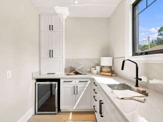 Discover this stylish wet bar featuring sleek white cabinetry, a built-in wine fridge, and a modern black faucet over a stainless steel sink.