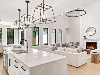 Experience modern luxury in this open-concept living space, featuring a sleek kitchen island with a waterfall countertop and a spacious living area with a cozy fireplace.