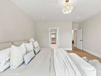 Experience serene comfort in this beautifully appointed bedroom, featuring a plush king-sized bed adorned with crisp white linens and an array of decorative pillows.