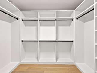Discover ample storage in this custom walk-in closet, featuring a sleek, modern design with white built-in shelving and black hanging rods.