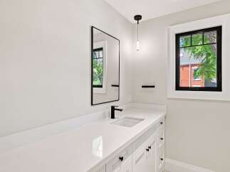 This modern bathroom features a sleek white vanity with black hardware, complemented by a minimalist black-framed mirror and a stylish pendant light.