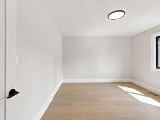 Step into this bright and airy room, featuring pristine white walls and elegant hardwood flooring that beautifully reflects the natural light.