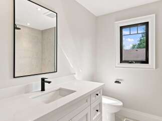 This modern bathroom features a sleek white vanity with a black faucet and a large, black-framed mirror reflecting a tiled shower.
