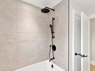 Experience modern luxury in this bathroom, featuring a sleek black shower system with both a rain showerhead and a handheld wand.