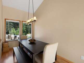 Enjoy meals with a view in this charming dining area, featuring a dark wood table and bench set against large windows overlooking a wooded landscape.