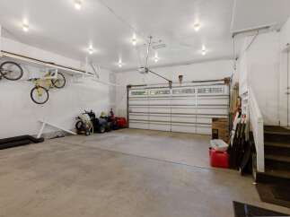 This spacious garage offers ample storage and organization solutions, featuring overhead racks for bicycles and a dedicated area for lawn equipment.