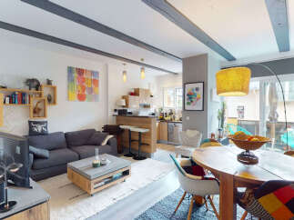 This open-concept living and dining area features a modern aesthetic with exposed wooden beams and a stylish grey sectional sofa.