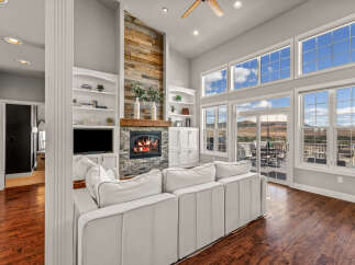 Experience luxury living in this stunning great room, featuring a rustic wood-accented fireplace and expansive windows that flood the space with natural light.