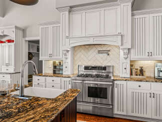 Experience luxury in this stunning kitchen featuring custom white cabinetry with beadboard detailing and elegant crown molding.