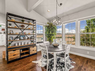 This dining area features a rustic industrial shelving unit and a round dining table with four chairs, all set against a backdrop of large windows offering scenic views.