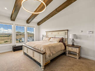 Experience rustic charm and modern comfort in this stunning bedroom, featuring vaulted ceilings with exposed wooden beams and a unique circular chandelier.