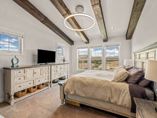 Experience rustic charm and modern comfort in this stunning bedroom, featuring exposed wooden beams and a unique circular chandelier.