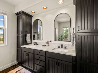 This modern bathroom features a sleek double vanity with black cabinetry and a white marble countertop, complemented by arched mirrors and black fixtures.