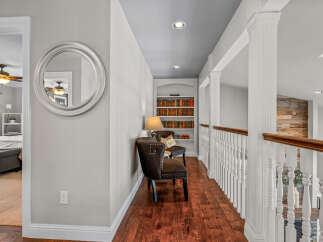 This spacious hallway features a built-in bookshelf filled with decorative books, complemented by two elegant armchairs and a stylish lamp.