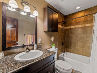 This bathroom features a granite-top vanity with a dark wood cabinet and a waterfall faucet, complemented by a large mirror with a decorative frame.