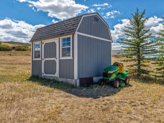 Discover this charming property featuring a rustic gray shed, perfect for storage or a workshop, complemented by a vibrant green John Deere riding mower.