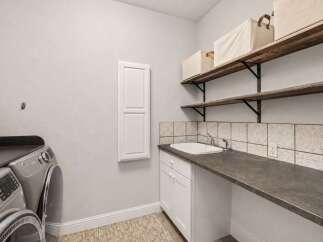 This laundry room boasts a practical layout with a front-load washer and dryer, complemented by a spacious countertop and sink area.