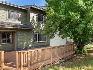 Enjoy outdoor living with this charming property featuring a spacious wooden deck and a large, mature tree providing ample shade.