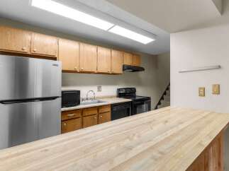 This kitchen features a full-size stainless steel refrigerator, a microwave, a double-basin sink, and a black electric range with an overhead vent.
