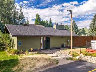 Discover this charming property featuring a well-maintained exterior with a green siding and a dark shingle roof, complemented by mature trees and lush landscaping.