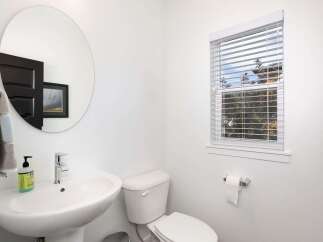 This bright and airy bathroom features a sleek pedestal sink with a modern chrome faucet, complemented by a round mirror reflecting a dark-paneled door and artwork.