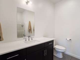 This modern bathroom features a sleek vanity with a white countertop and dark cabinetry, complemented by a large mirror and chrome fixtures.
