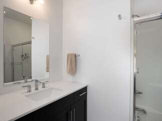 This modern bathroom features a sleek vanity with a white countertop and a dark cabinet, complemented by a large mirror and chrome fixtures.