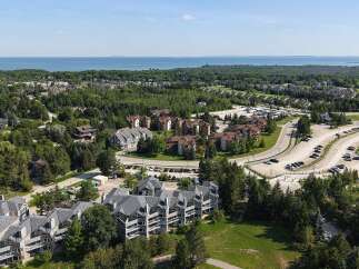 Discover this stunning aerial view showcasing a modern residential complex nestled amidst lush greenery and overlooking a serene body of water.