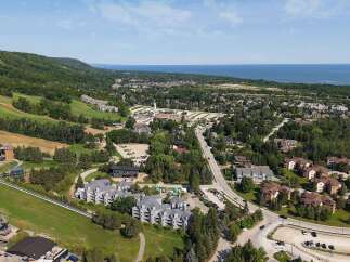 Discover this stunning aerial view of a vibrant community nestled amidst rolling green hills and overlooking a serene blue lake.