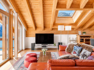 Experience breathtaking mountain and lake views from this stunning living room, featuring a vaulted wood-beamed ceiling and a large skylight.