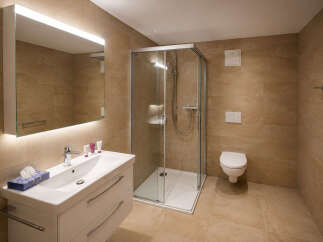 This modern bathroom features a spacious walk-in shower with glass enclosure and a sleek vanity with a large illuminated mirror.