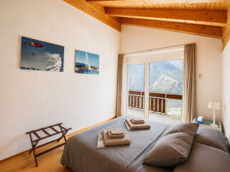 Experience breathtaking mountain views from this charming bedroom, featuring a cozy bed and a private balcony perfect for enjoying the alpine scenery.