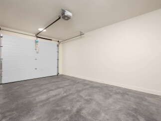 This spacious garage features a clean, modern aesthetic with a white sectional garage door and a smooth concrete floor.