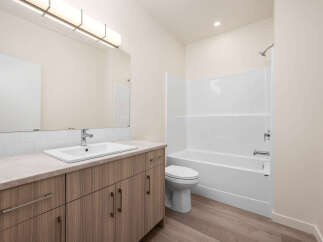 This modern bathroom features a sleek vanity with ample storage and a clean white sink, complemented by a large mirror and contemporary lighting.