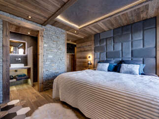 Experience rustic luxury in this mountain-inspired bedroom, featuring a striking stone accent wall and warm wooden beams.