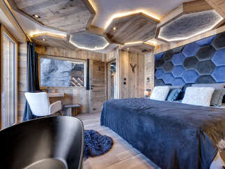 Experience luxury mountain living in this stunning bedroom featuring a unique hexagonal upholstered headboard and a dramatic wood-paneled ceiling with integrated lighting.