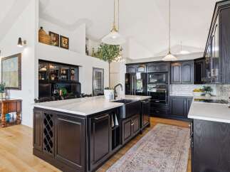 Experience luxury in this stunning kitchen featuring sleek black cabinetry and a large marble-topped island with a farmhouse sink.