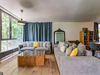 Experience modern living in this spacious living room, featuring a large sectional sofa adorned with colorful throw pillows and a unique wooden coffee table with a glass top.