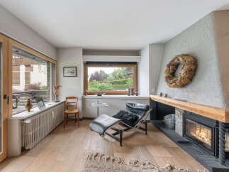 Experience cozy living in this inviting room featuring a modern fireplace with a rustic wooden mantel and a large window offering scenic views.